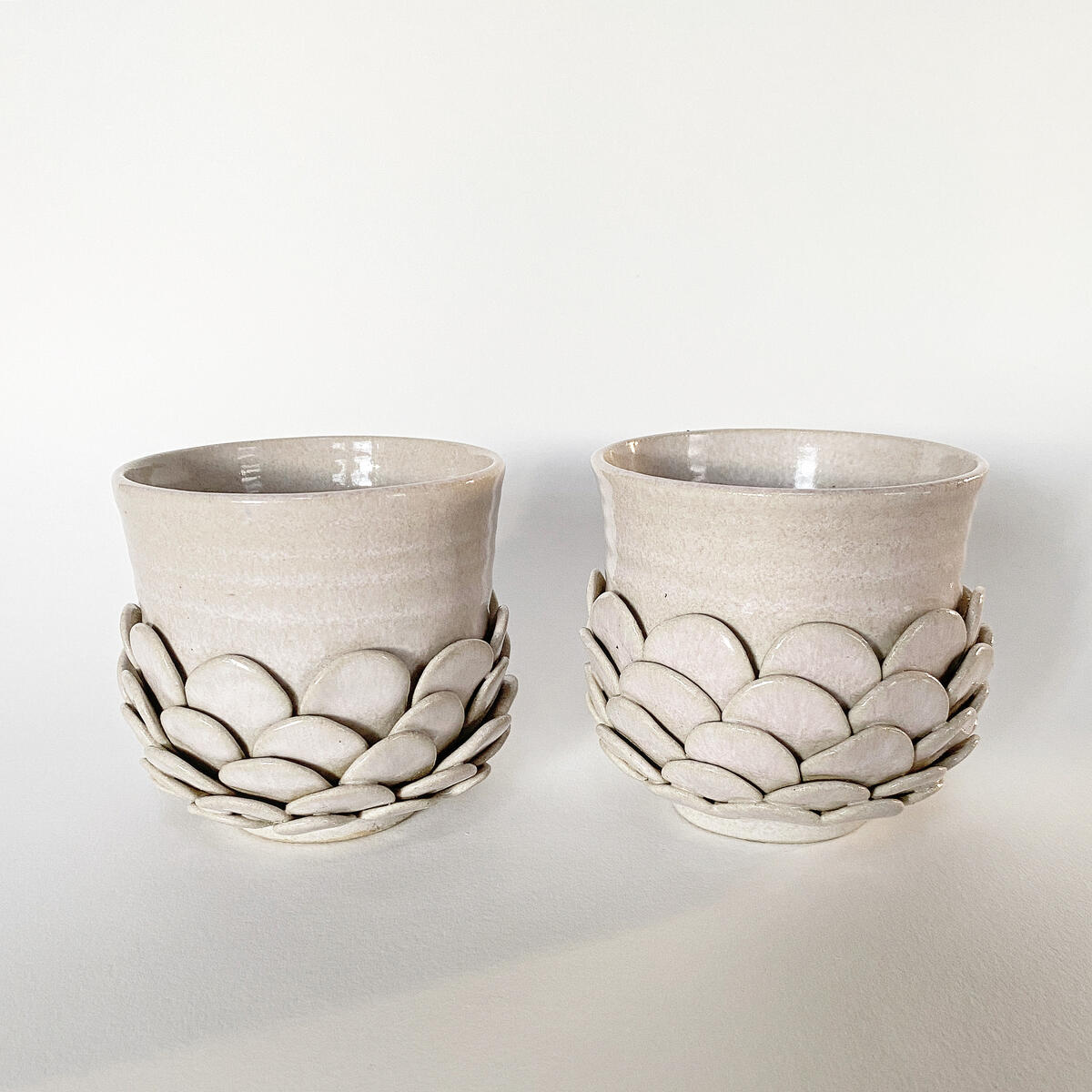 “Safe Mugs” Ceramic Cups — handcrafted relief texture in creamy white by Natty Ceramics atelier in Utrecht Two handcrafted ceramic mugs from the “Safe Mugs” collection with scaled relief texture like overlapping petals, glazed in creamy white